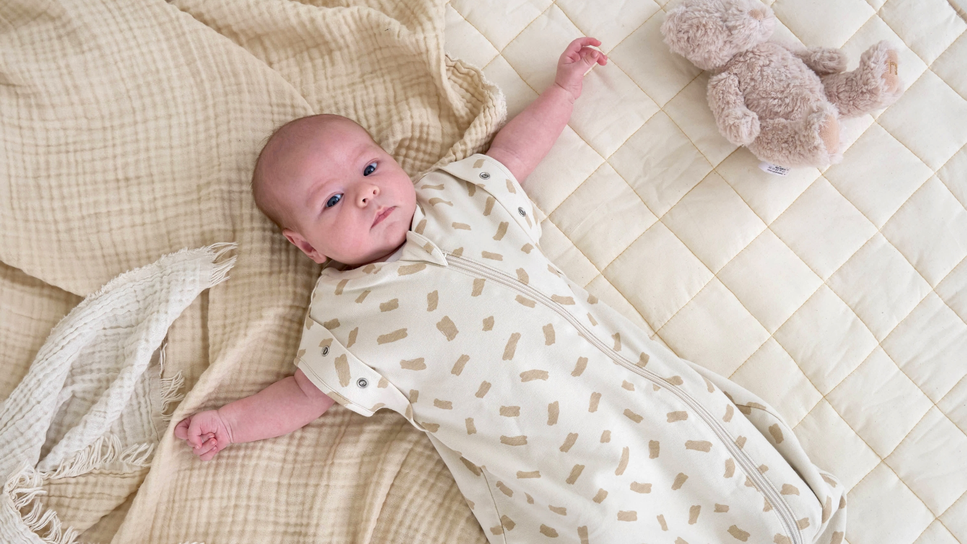 Baby in the Little Dreamers Dash Organic Sleeping Bag (0-3 Months) playing in a grey cot bed | Baby Sleep Bags, Shawls, Swaddles & Sleepbags | Nightwear | Nursery - Clair de Lune UK