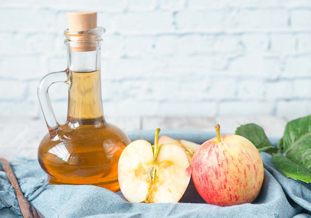 Kleine Glasflasche mit Apfelessig, daneben ein aufgeschnittener Apfel.