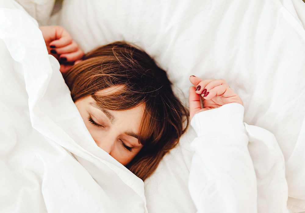 Frau schläft zugedeckt unter einer weißen Decke.