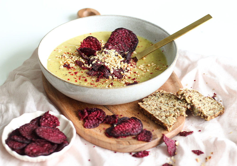 Birnen-Selleriesuppe mit Betechips in einer grauen Porzellanschüssel. Darunter liegt ein gelbes Seidentuch. Drumherum liegen Rote Beete Chips verteilt.