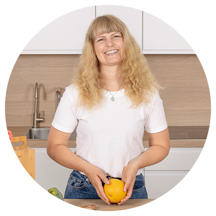 Blonde Frau steht in einer Küche und hält eine Orange in den Händen