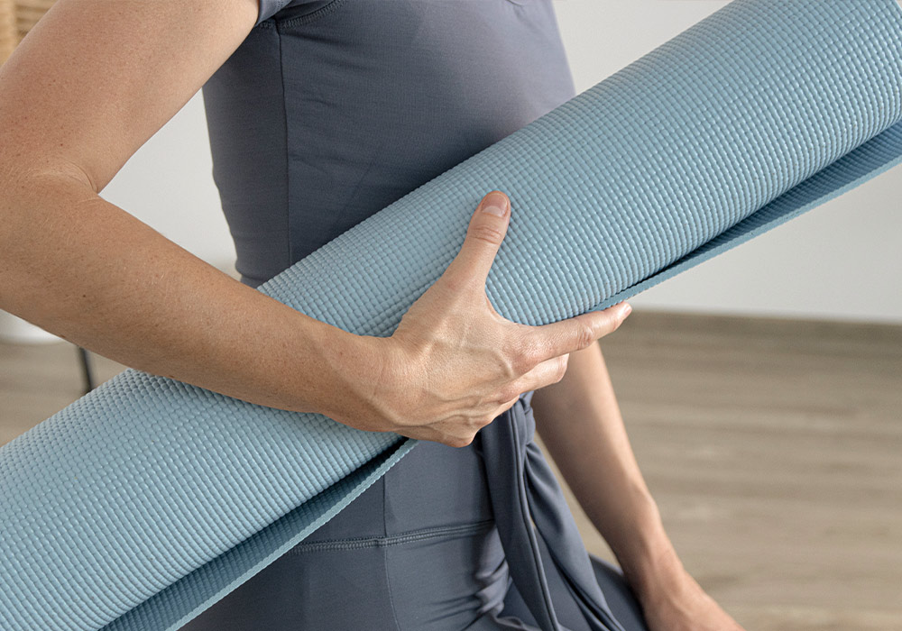 Eine Frau hält eine blaue Yogamatte unter dem Arm.