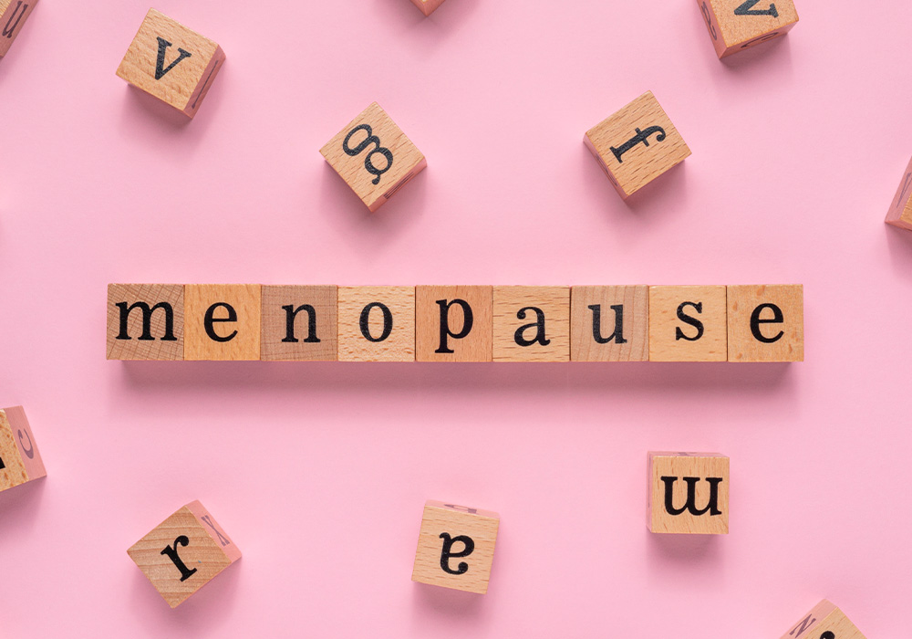 Auf einem rosa Untergrund liegen Holzbausteine und bilden das Wort menopause.