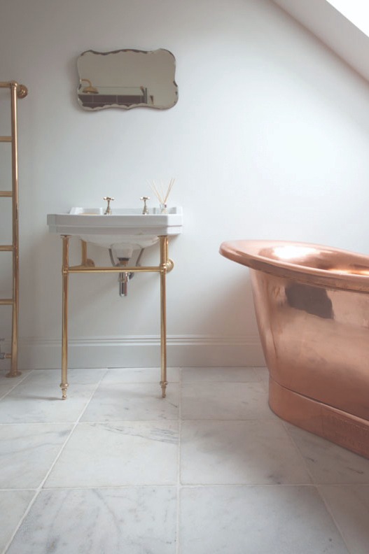 Modern bathroom tile inspiration showing Parisian White tumbled marble tiles on the floor beneath a copper bath, highlighting natural veining and a sophisticated, contemporary aesthetic.