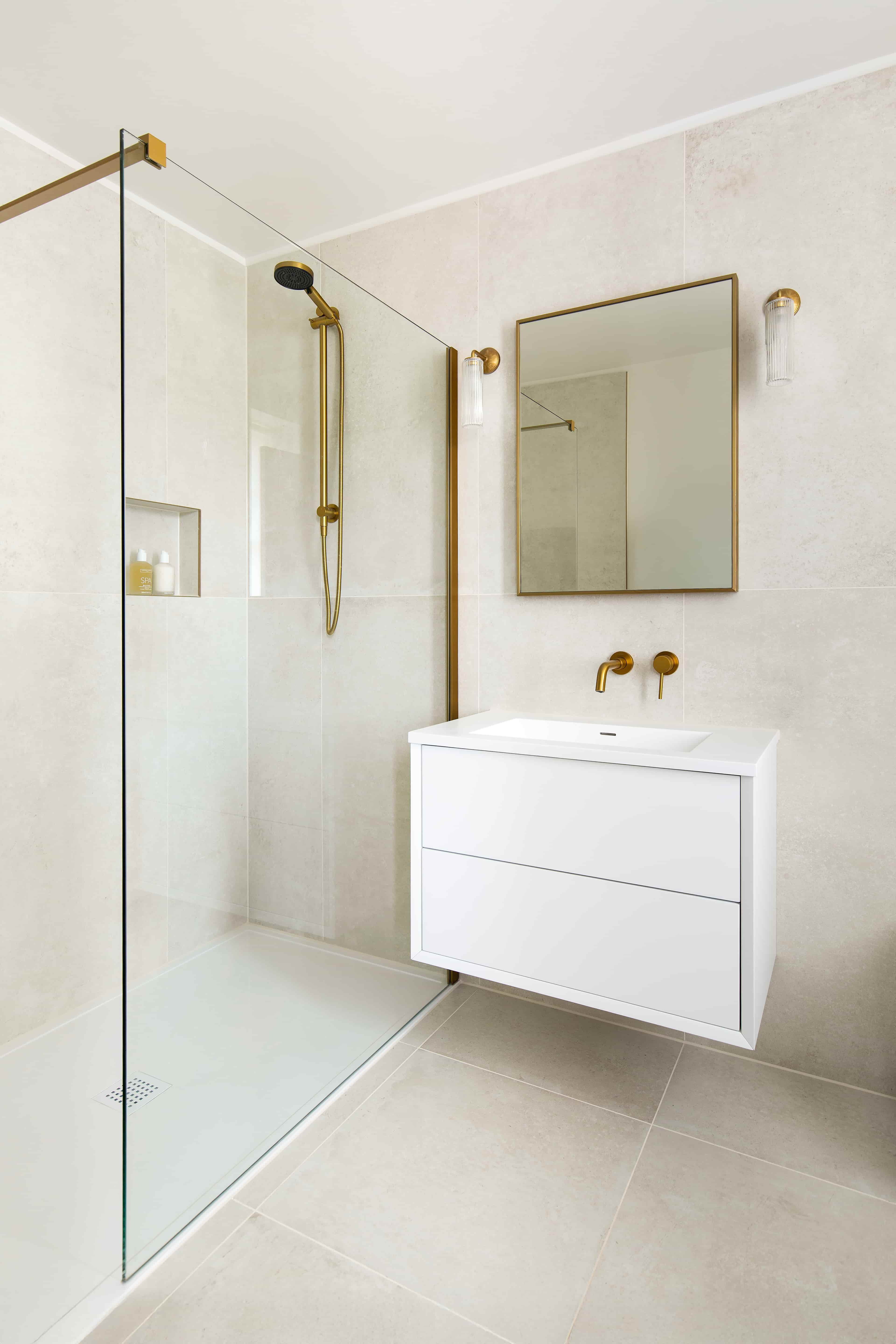 A modern style bathroom with white cabinets, a gold mirror and a gold shower.