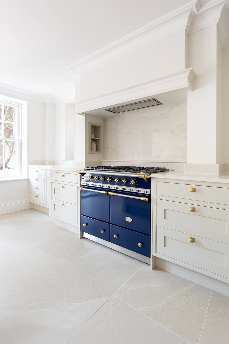 A corner of the kitchen with white cabinets, an ivory tiled floor and a navy blue cooker.