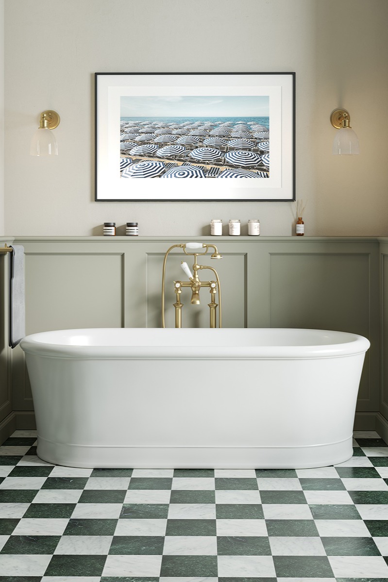 Elegant bathroom featuring a white freestanding bathtub, brass fixtures, and a Riviera Emerald and White chequerboard floor. Wall art and sconces add a serene, luxurious feel.