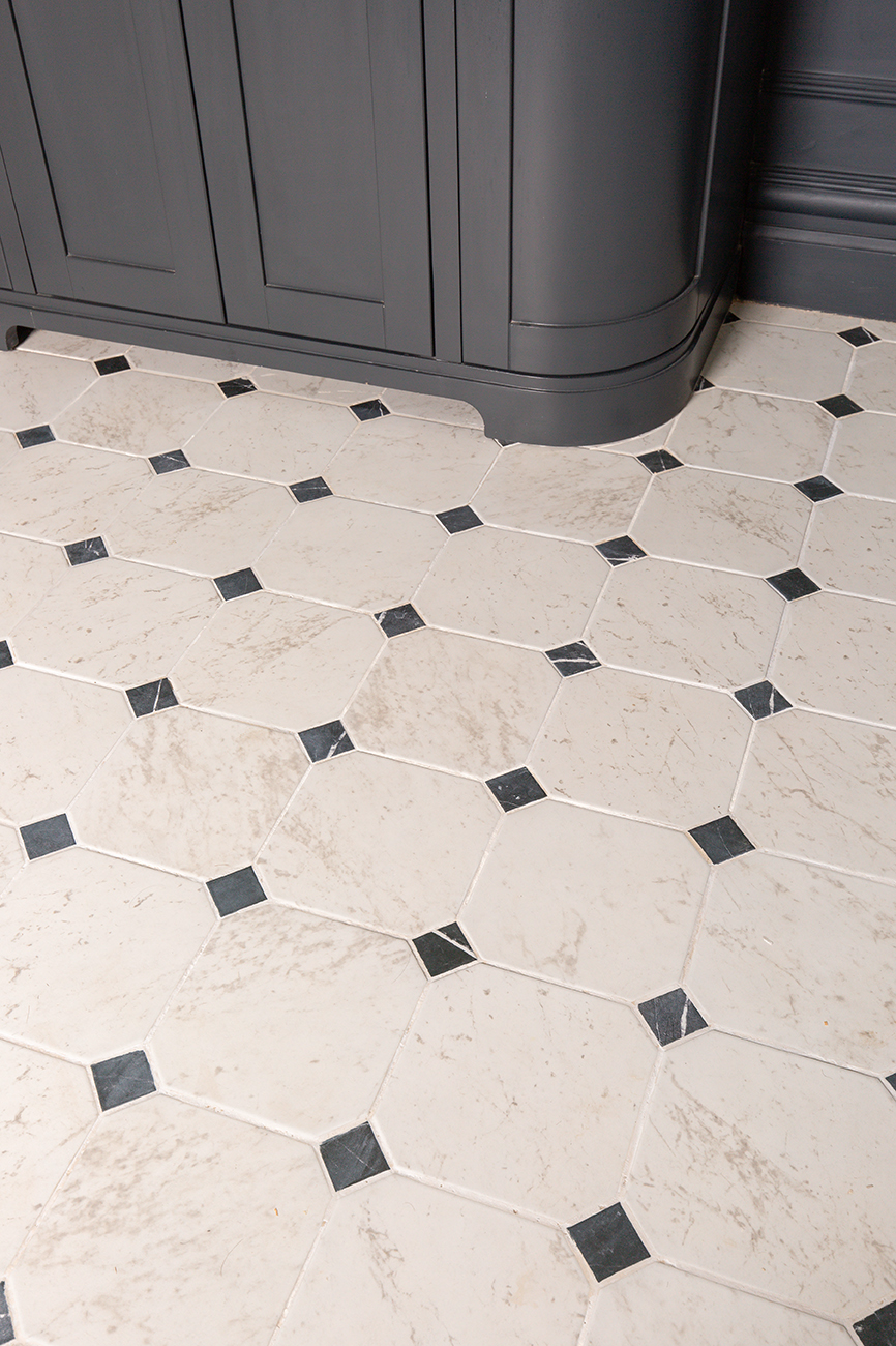 Corner of dark grey bathroom vanity unit with pale limestone tiles.
