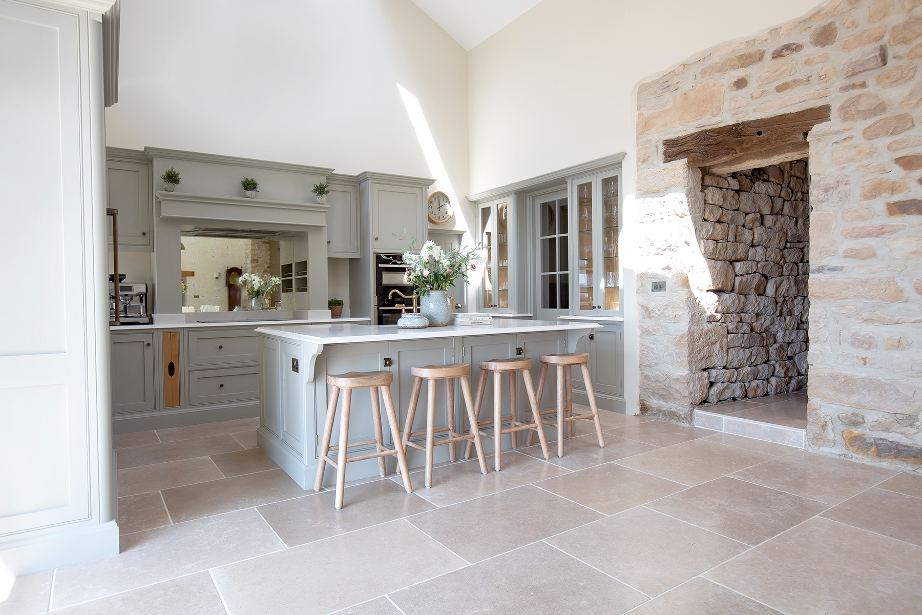 country kitchen barn conversion with exposed stone and dijon limestone floor tiles with pale blue kitchen island and wooden stools