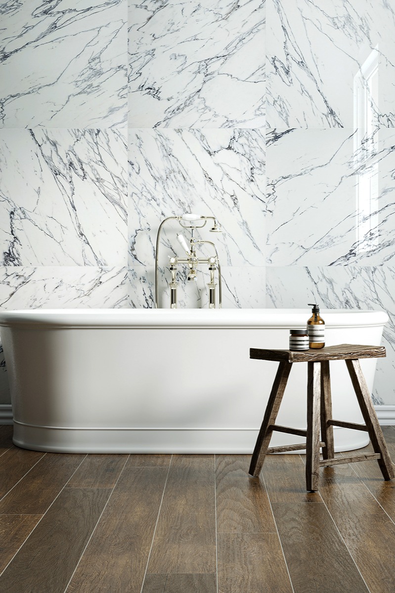 Luxurious bathroom with white marble wall, freestanding white bathtub, rustic wooden stool, and chatsworth tudor oak effect dark wooden floor, creating a serene and elegant atmosphere.