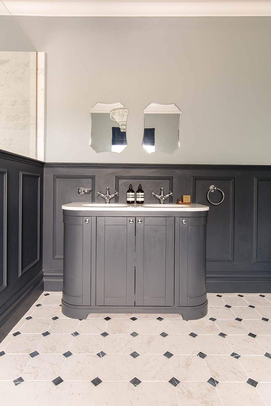 A large dark grey bathroom vanity unit with matching panelled walls and a limestone tile floor.