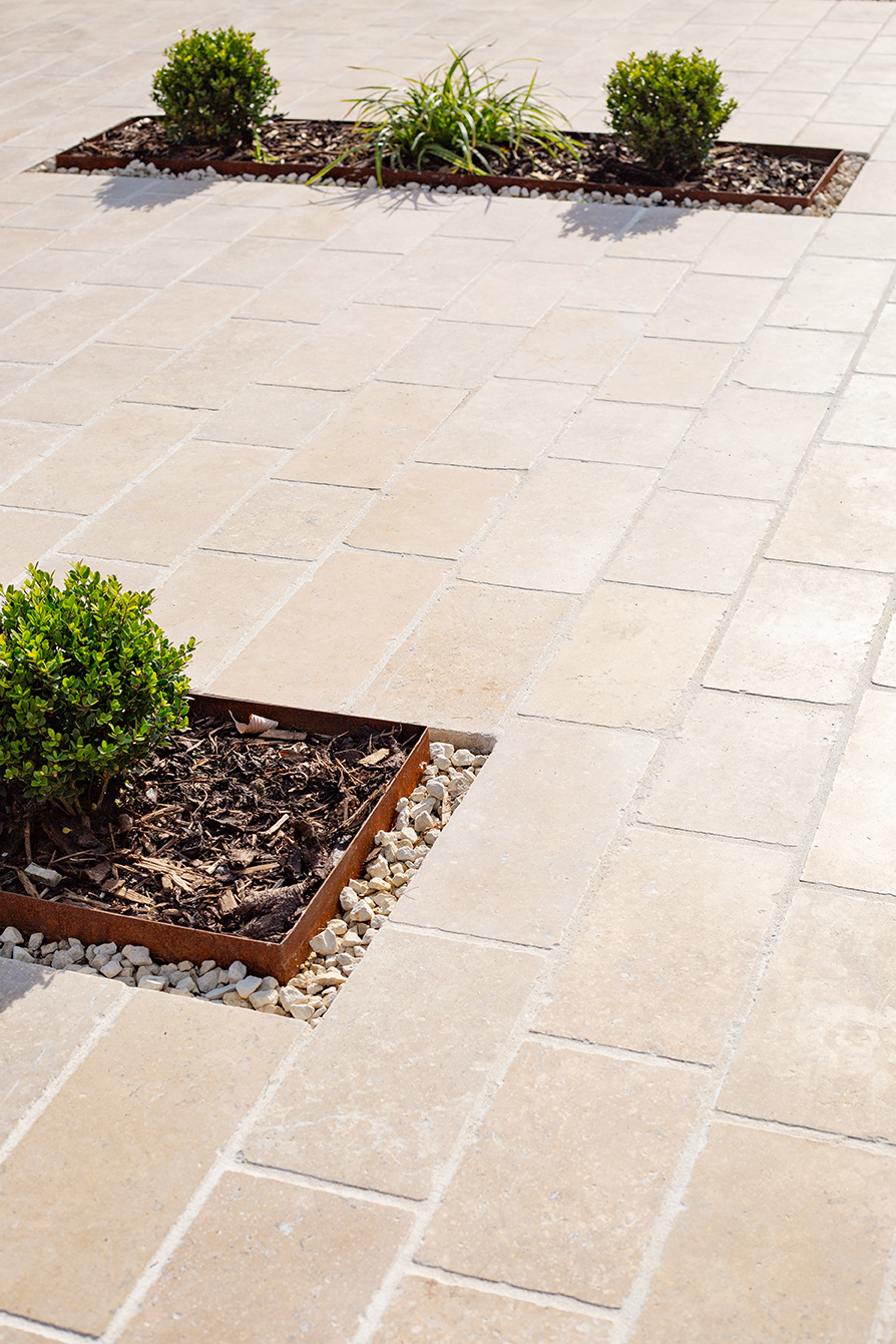 A beige paving outside patio floor with built in flower beds.