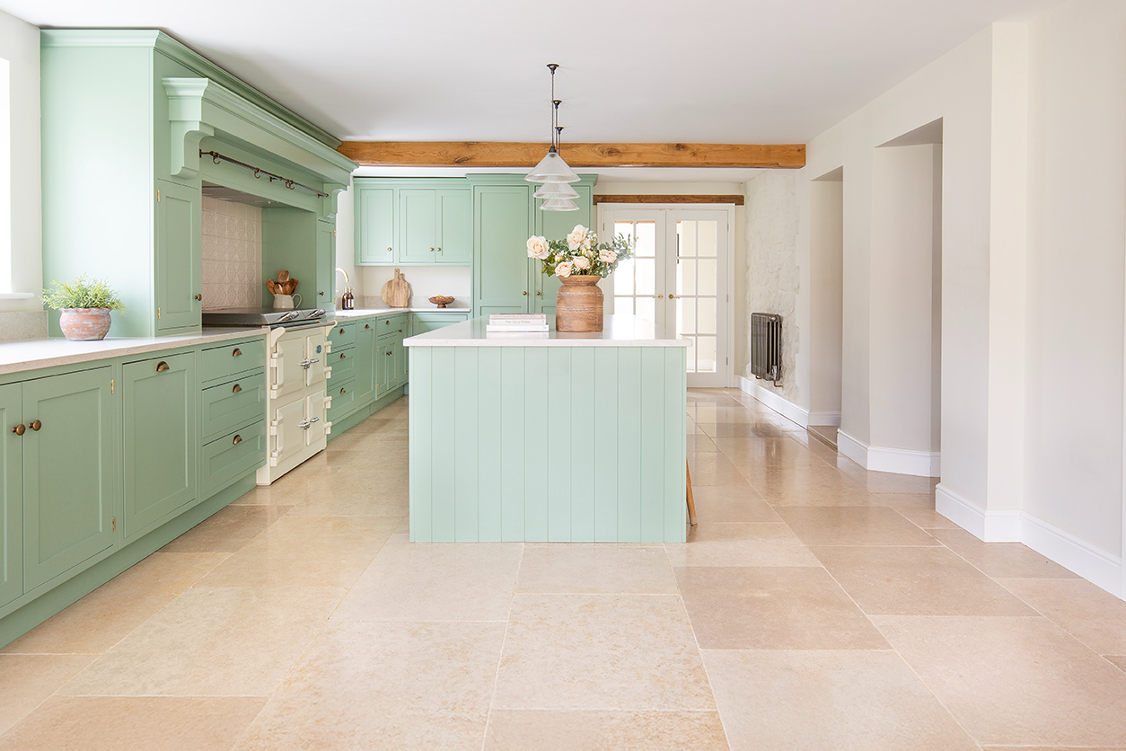 A large French inspired kitchen, featuring light green cabinets and a large island, with a limestone floor.