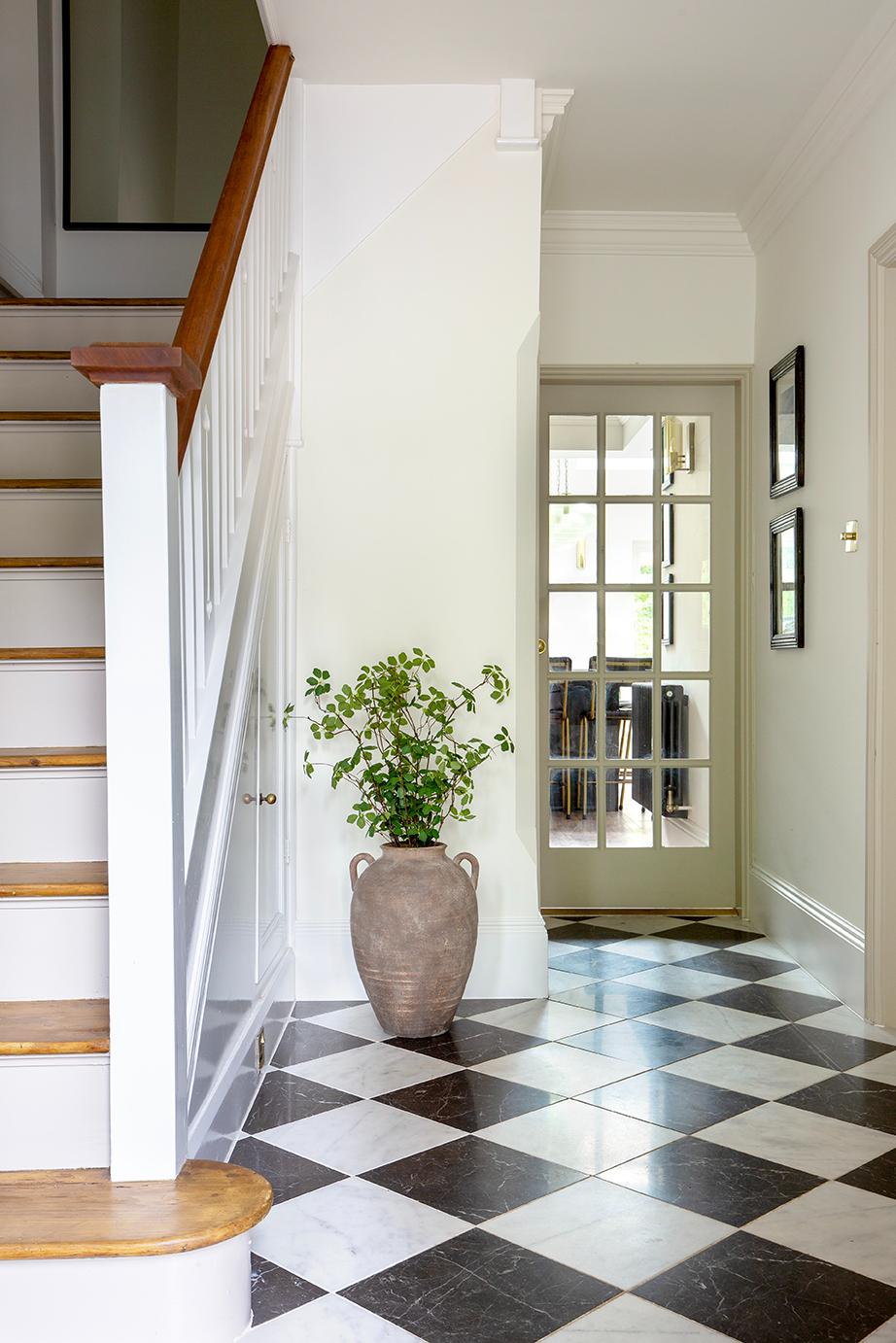 Riviera Black and White Honed marble flooring in a hallway, featurinf a large terracotta vase and wooden stairs 