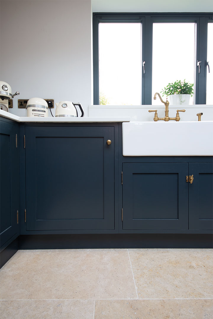 Dijon Tumbled floor in kitchen with navy blue units with white work top 