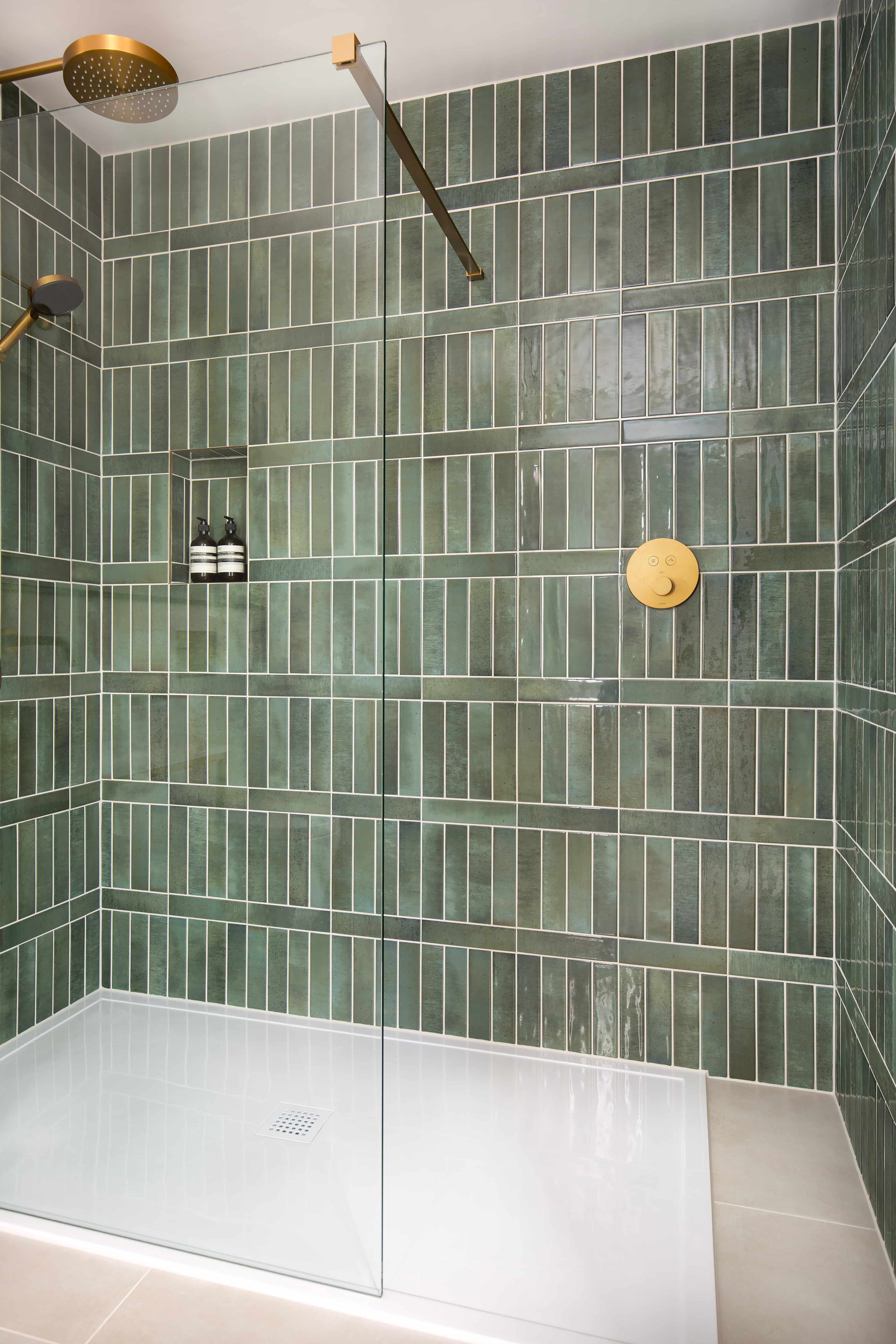 A large shower cubicle with a white shower tray and green zellige tiles on the wall.