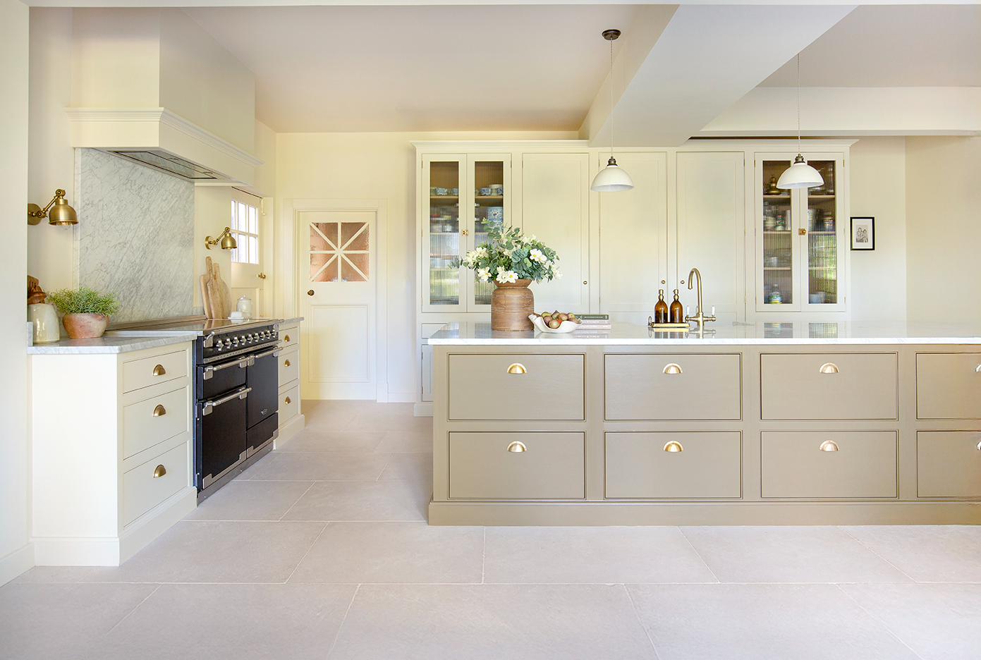 A large, modern kitchen featuring a spacious island, cream display cabinets with glass windows and a marble splashback.