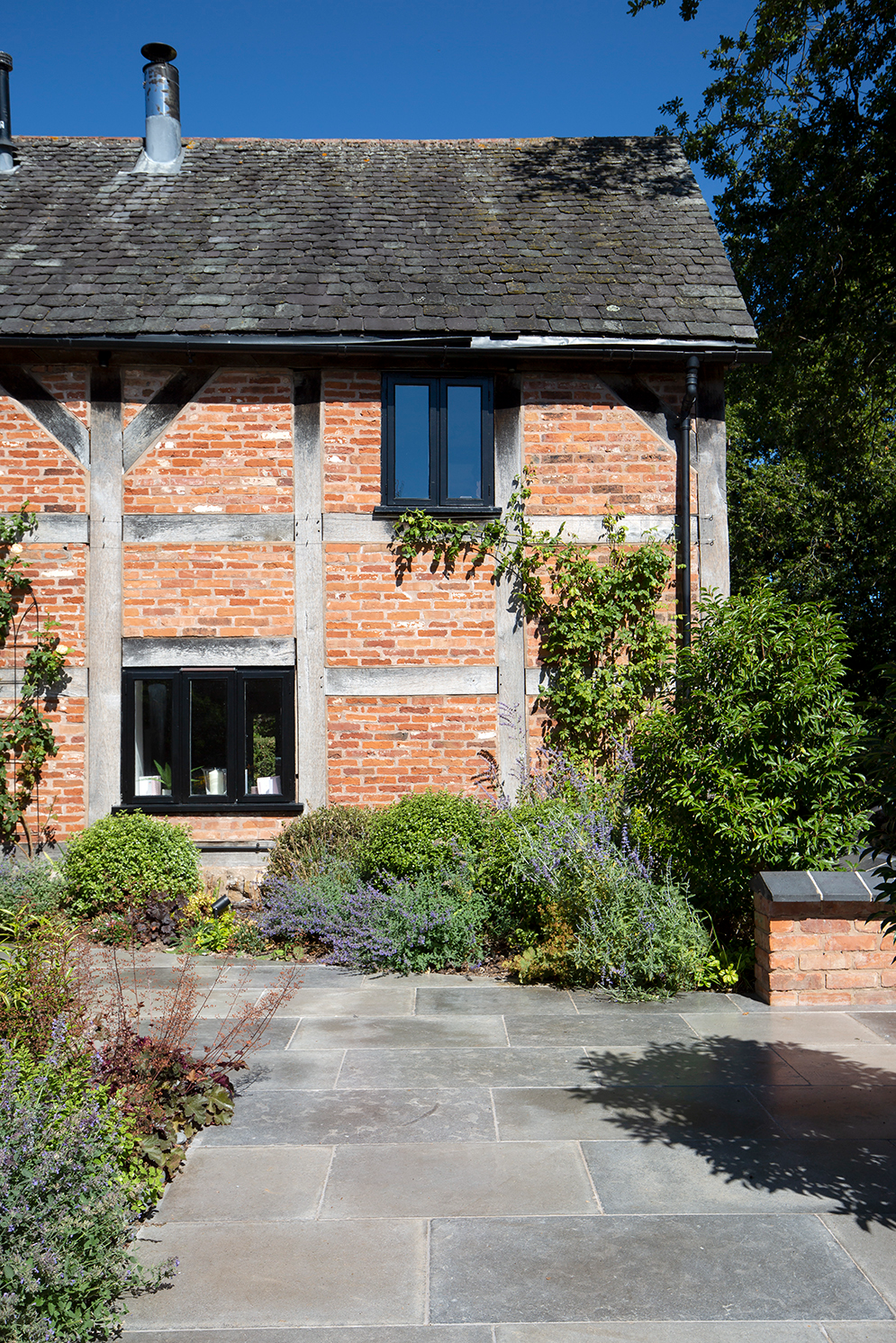 Farrow Grey Tumbled Outdoor Pavers with a tudor brick house and flower beds 