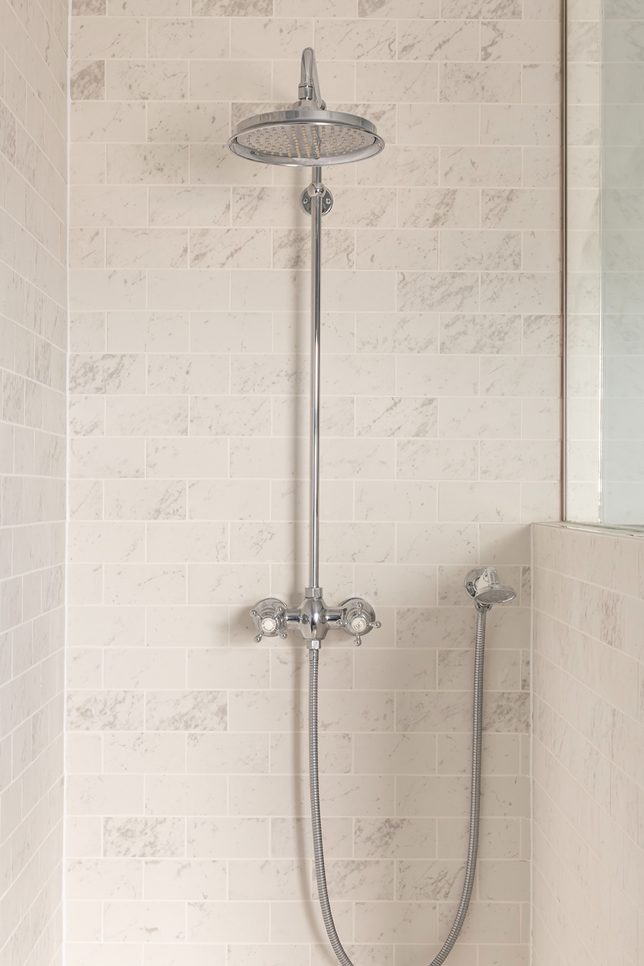 A chrome shower head in a shower with white marble tiles.