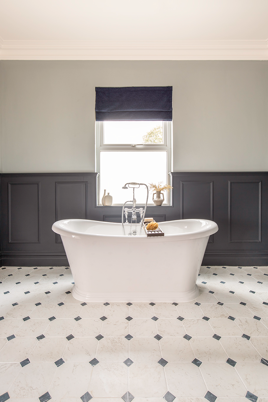 A large, modern bathroom featuring a white freestanding bath and a limestone tiled floor.