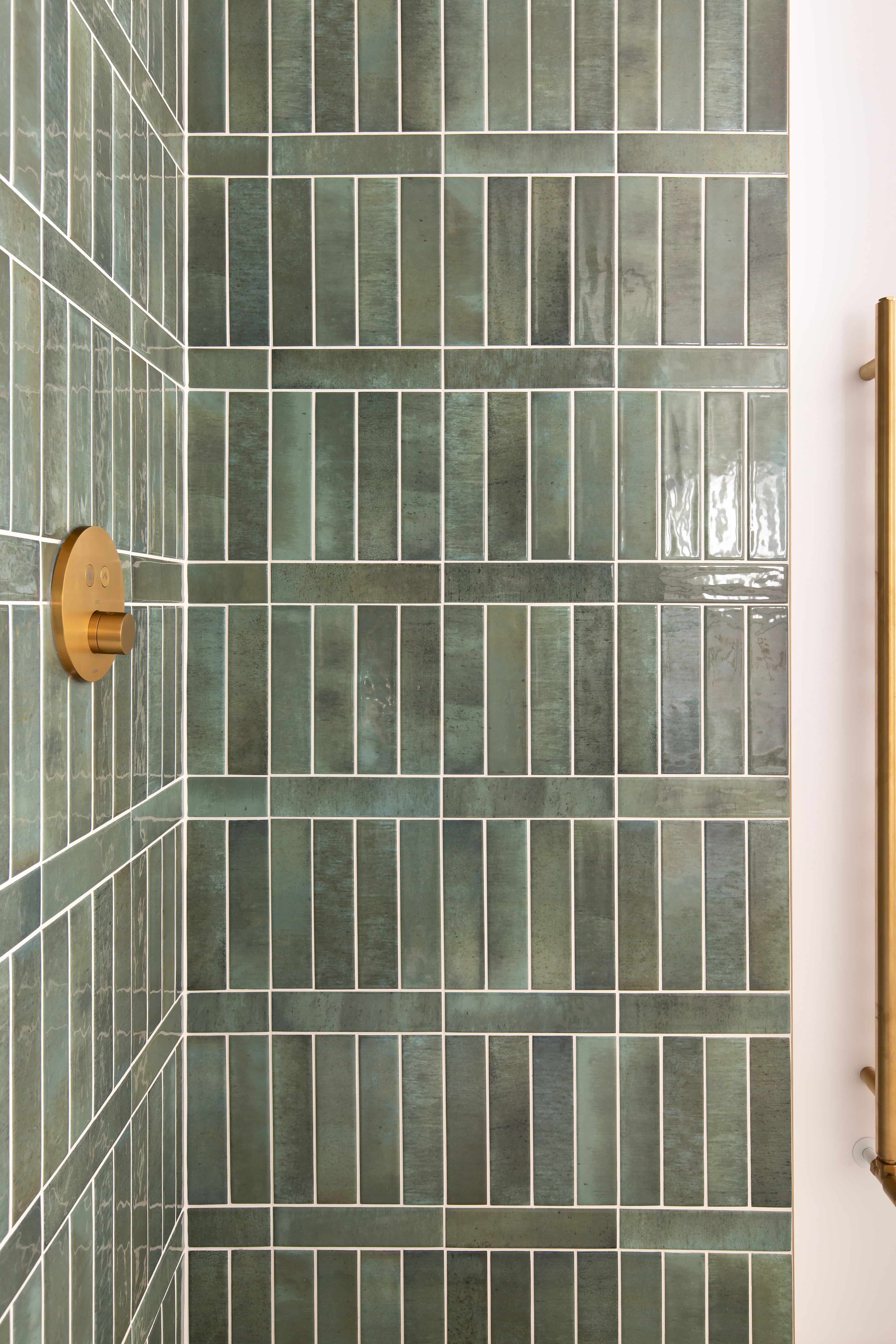 A shower cubicle with dark green zellige tiles on the wall and gold accents, including a hand rail.