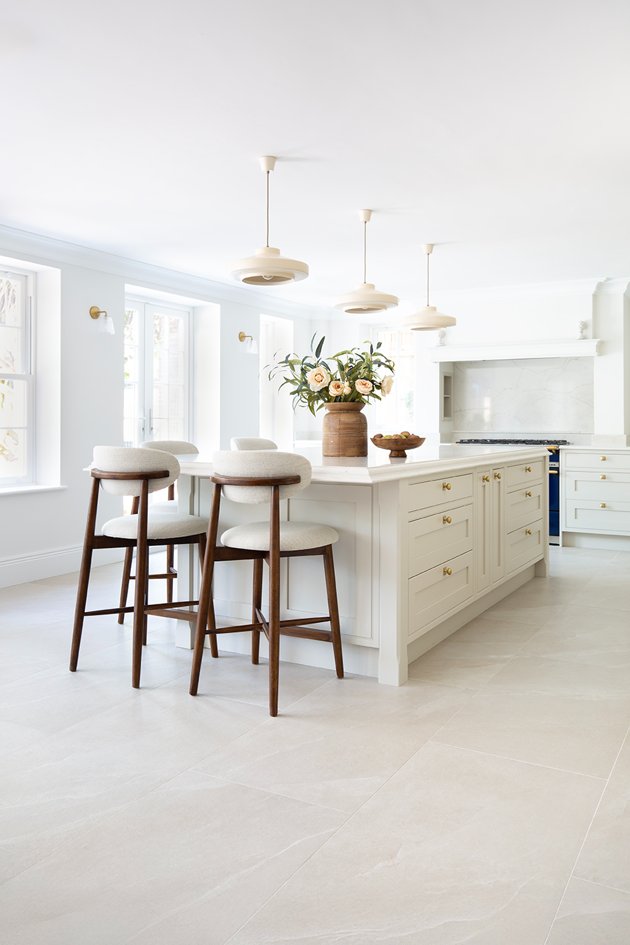 A bright, large kitchen with white cabinets and an island in the centre, featuring dark brown wooden bar stools.