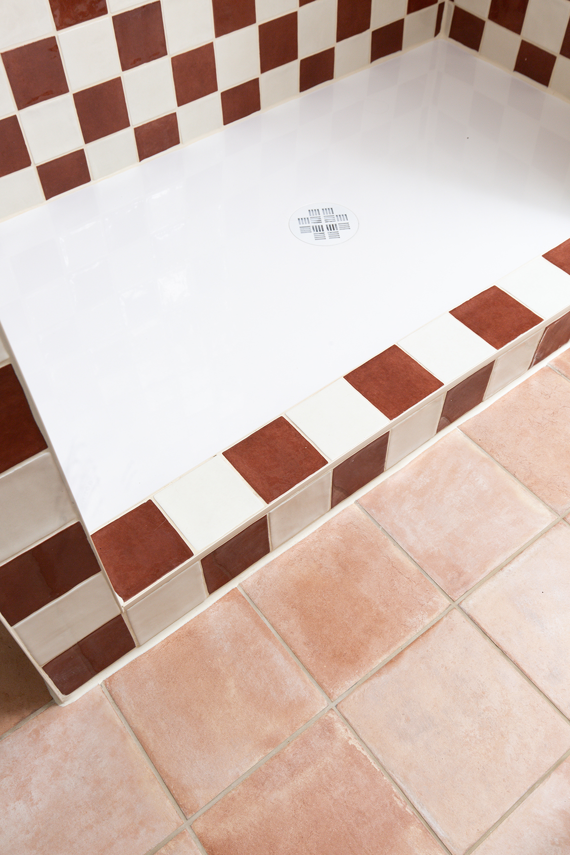 Shower area with red and white checkered tiles, and a white basin with a central drain. Terracotta Campello Rosato floor tiles add a warm, rustic feel.