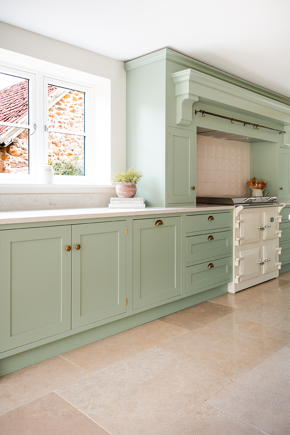 A corner view from a green pastel kitchen, a white cooker and beige limestone tile flooring.