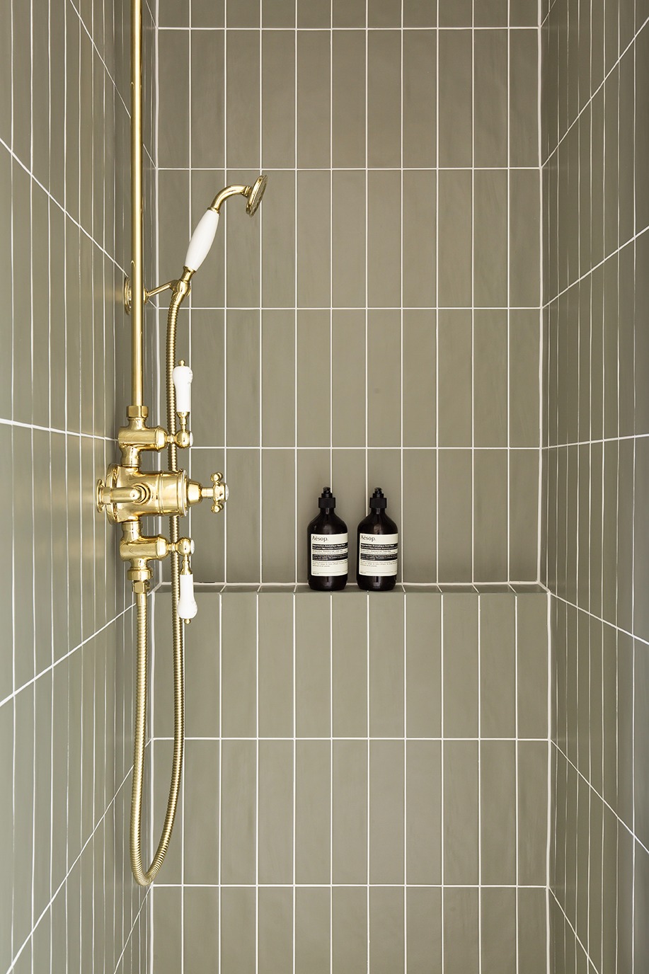 Close-up of Orkney Green metro tiles paired with a gold shower, highlighting deep green tones and sleek matt finish for modern bathroom tile inspiration.
