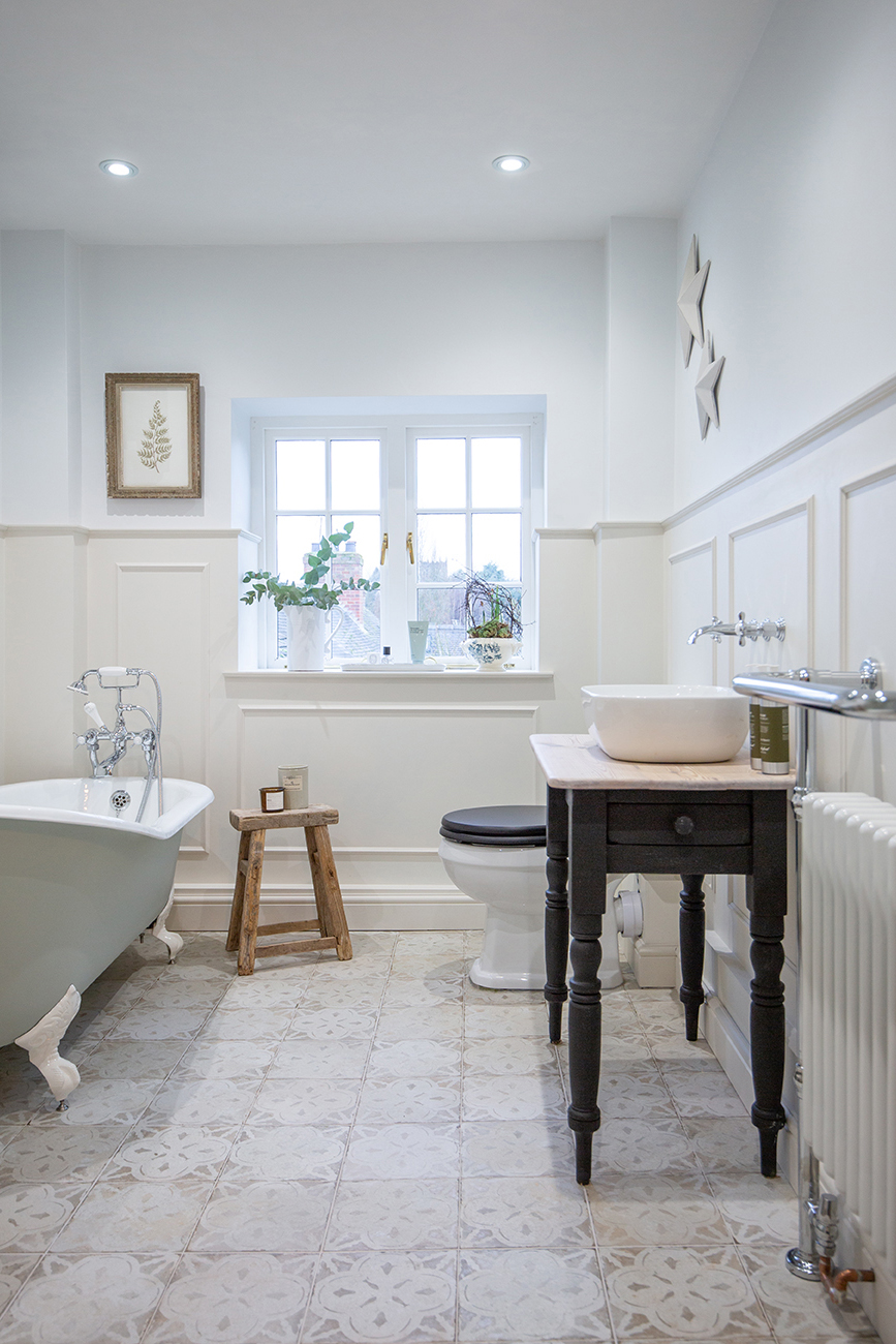 Bright bathroom featuring a white clawfoot tub, wooden stool, black vanity with a white basin, and plants on the window ledge. Relaxed ambiance featuring Ophelia White tiles.