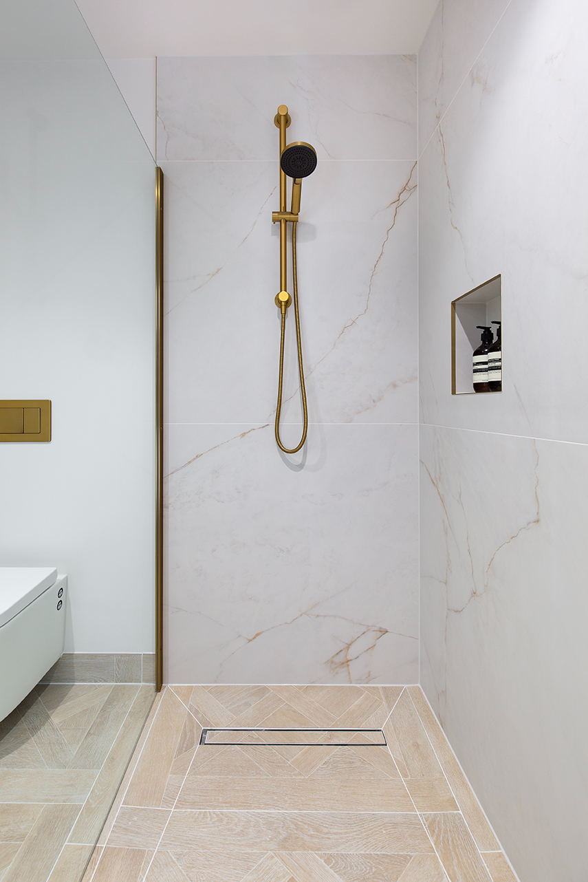A large shower cubicle with white marbled tiles on the wall and light wooden parquet flooring as a shower tray.