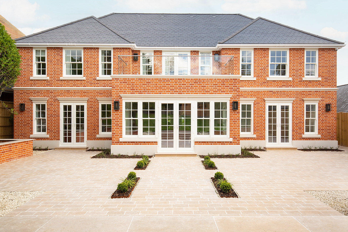 A large Georgian-inspired, new build home with a paved driveway and large windows.