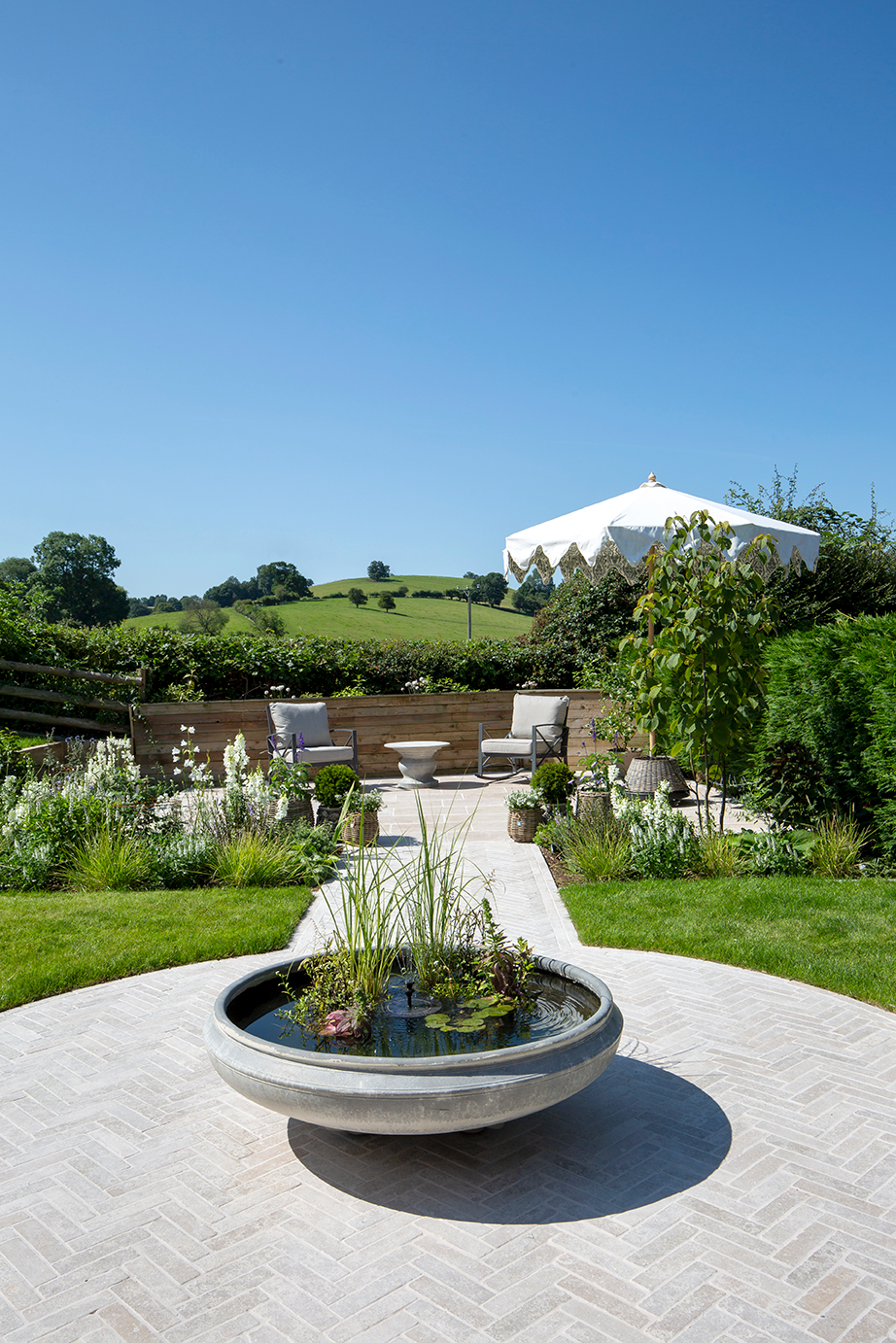 A garden with a water decorative and Dijon tumbled herringbone pavers