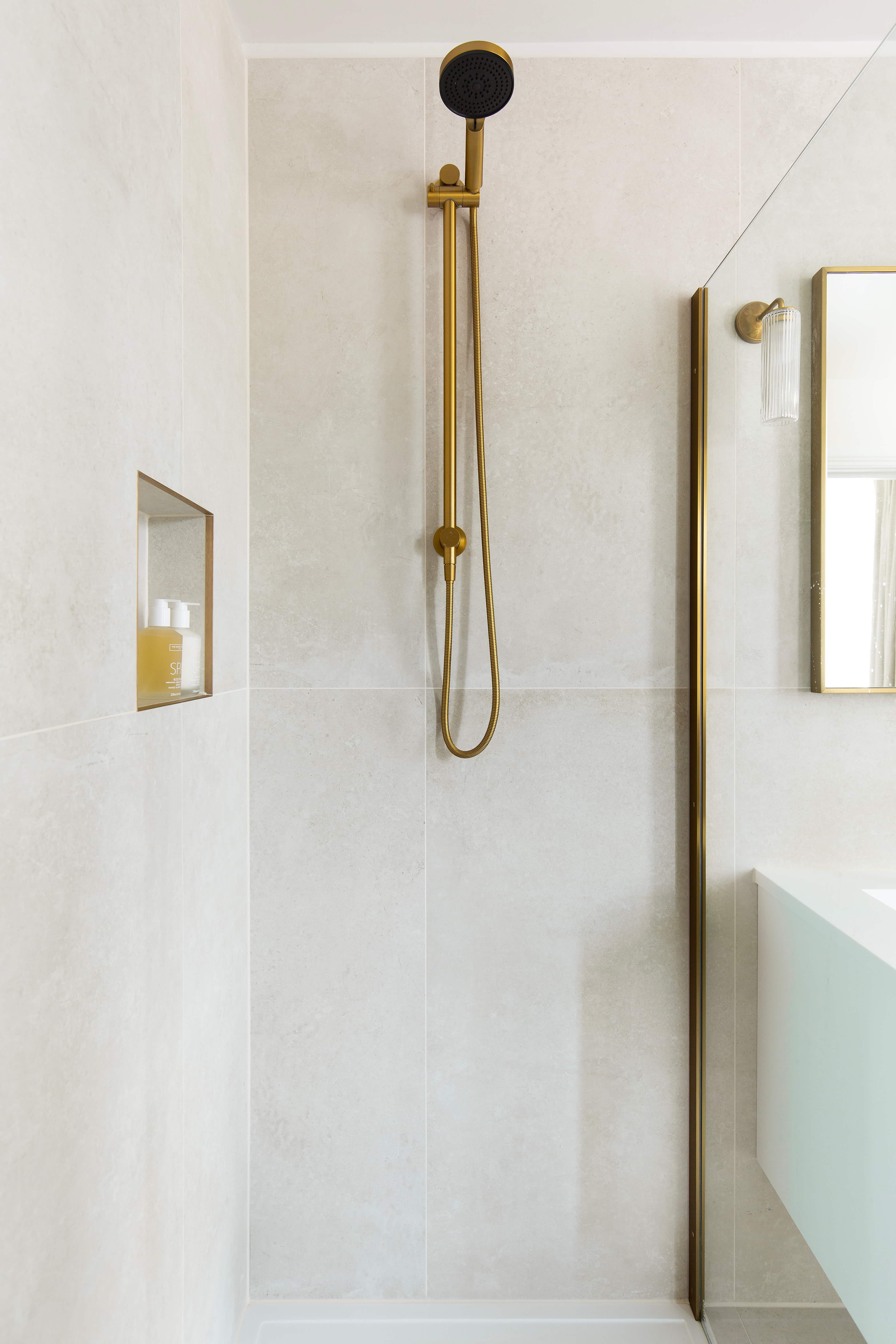 A neutral toned bathroom with ivory tiles on the wall and a gold shower with a glass screen.