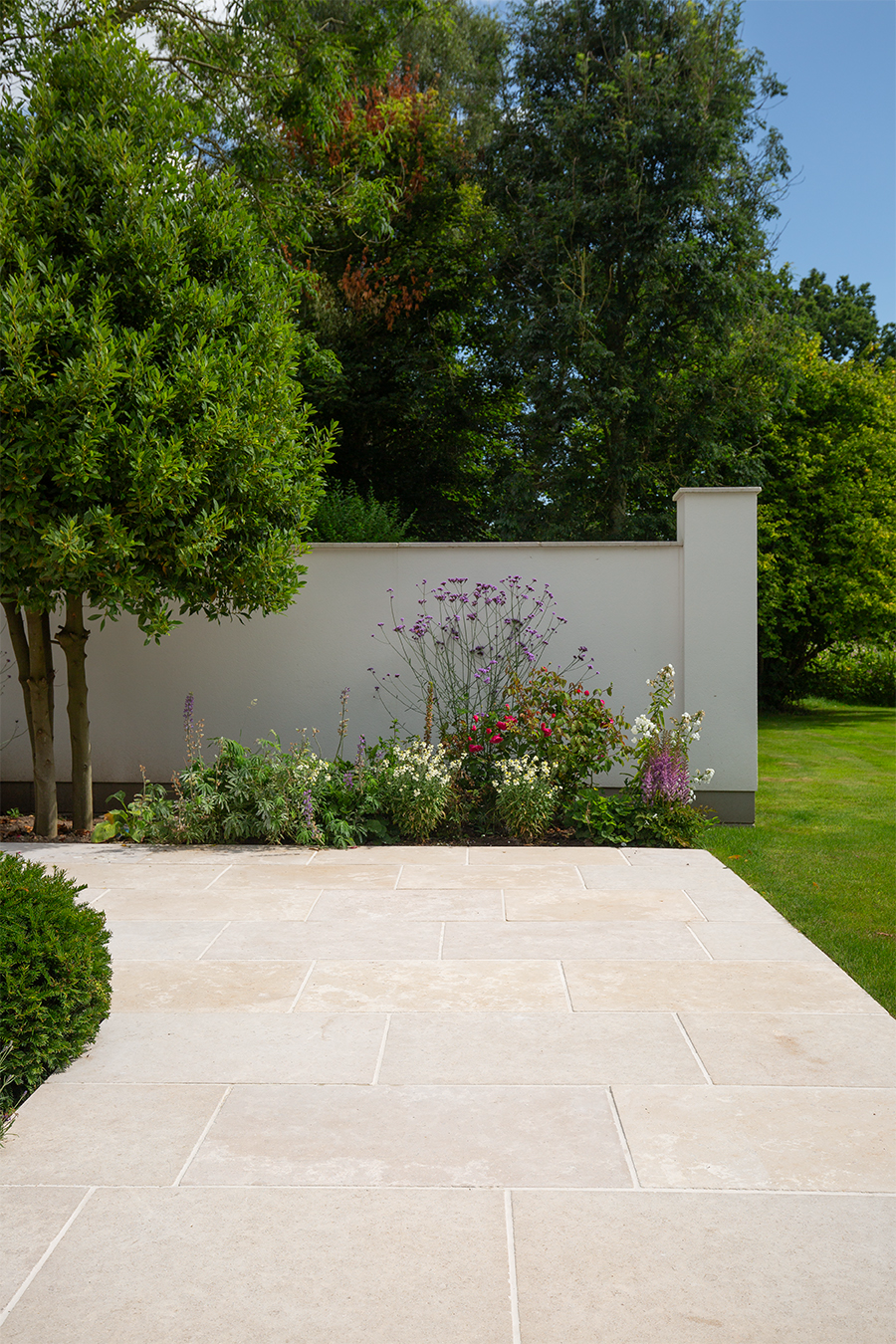 A white wall with a Dijon Tumbled walkway and trees
