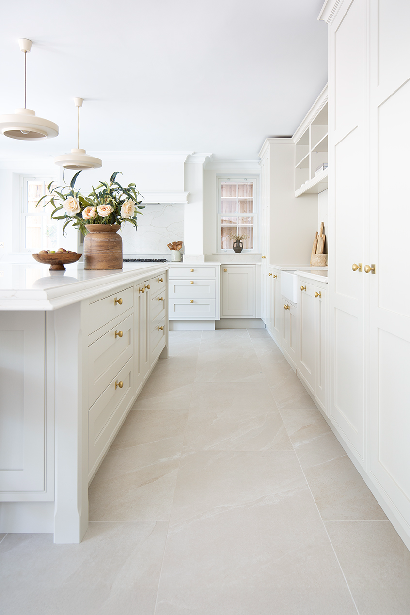 A bright, light kitchen area with white cabinets and an ivory tiled floor.